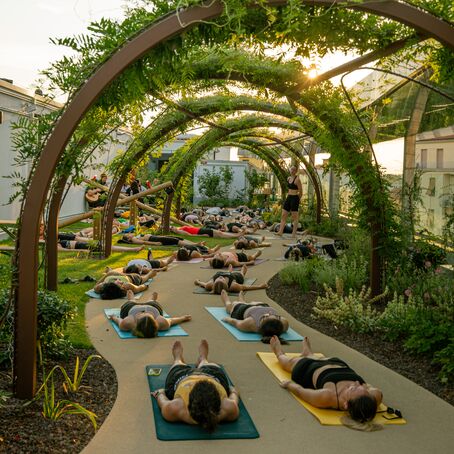 Outdoor group yoga session under leafy arches in garden at sunset