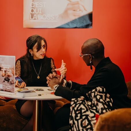 Two people in focused discussion at small table against bold red wall