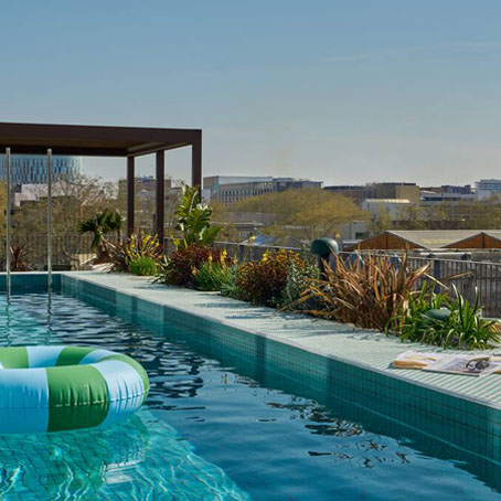 A rooftop swimming pool at The Social Hub Barcelona with a rubber ring floating inside and a nice view of the city